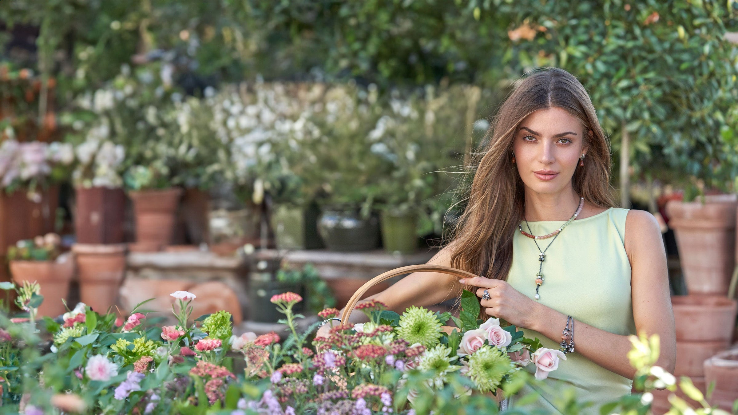 Model standing in a garden with a basket full of flowers, wearing Trollbeads Jewellery